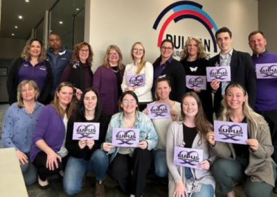 Team members from Duliban Insurance Brokers wearing purple and holding a lupus awareness sign in support of Support Lupus Day.