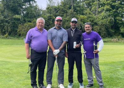 A group of men at a charity golf tournament, some wearing purple, gathered in support of lupus awareness.