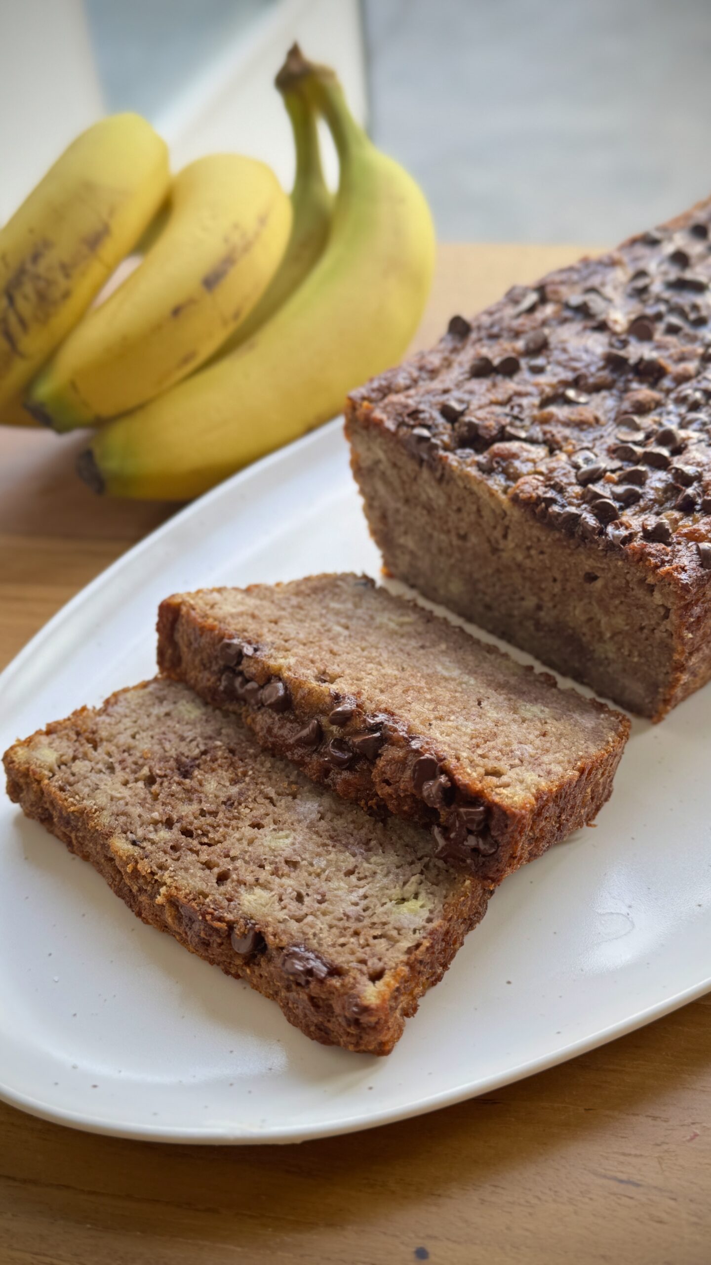 Sliced AIP banana bread made with coconut flour, topped with dairy-free chocolate chips on a cooling rack