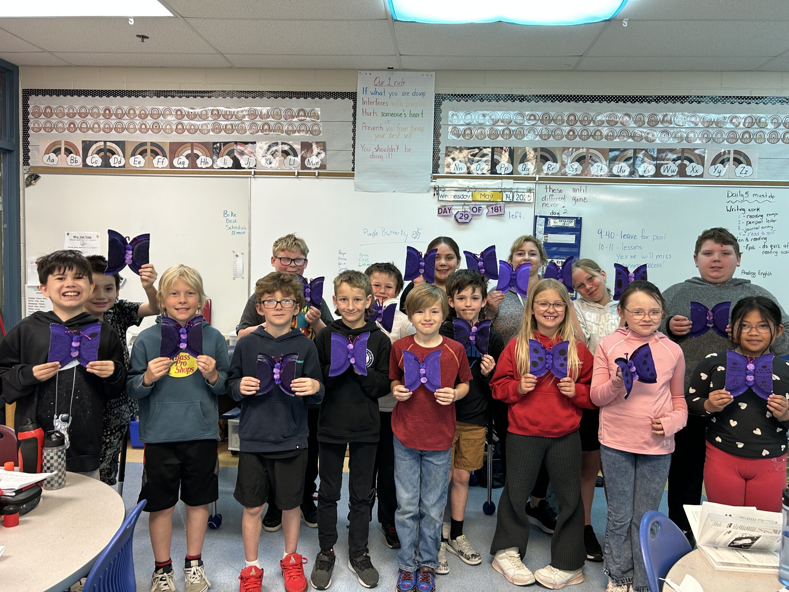 A group of students from École Springfield School smile and hold up handmade purple butterfly crafts for lupus awareness.