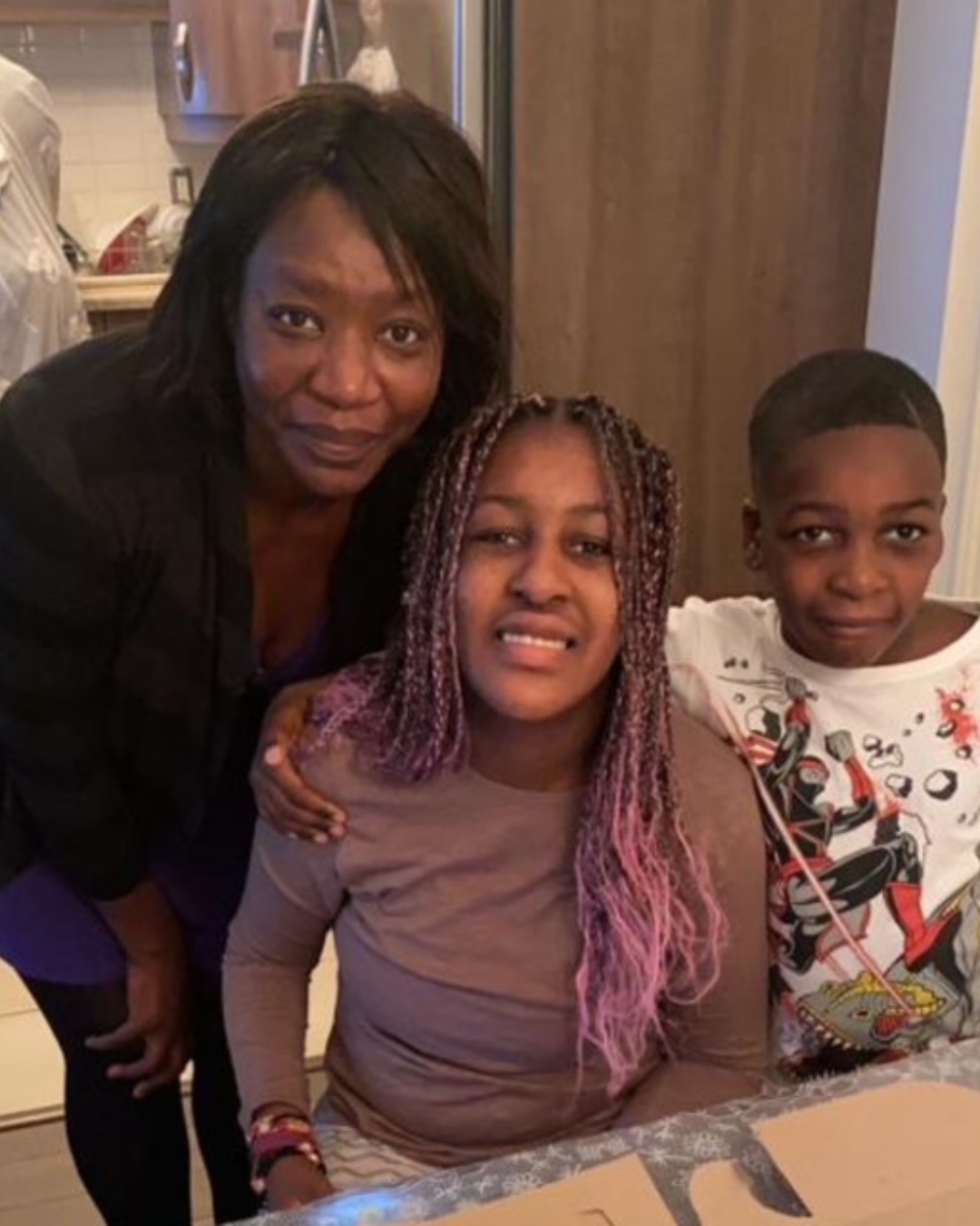 Anita Toni smiling indoors with her arms around her daughter and son, gathered at the family table.