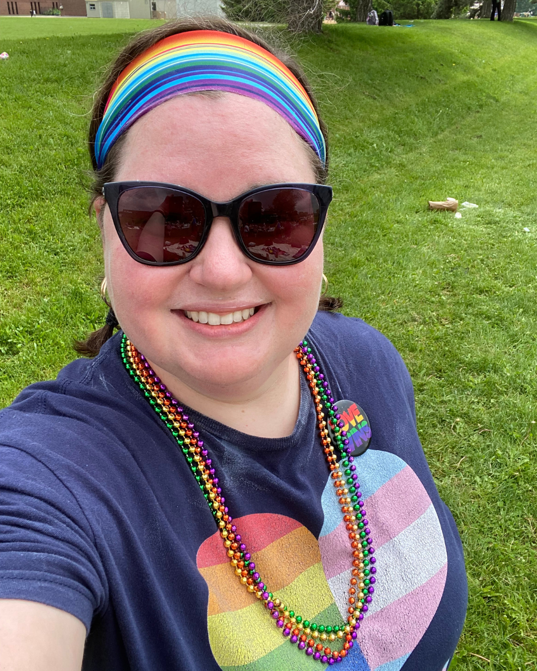 Megan Friedman smiling outdoors wearing a rainbow shirt and headband at a community event.