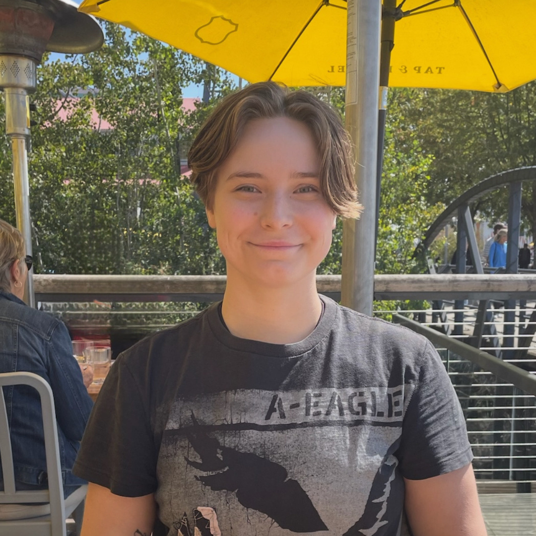 Portrait of Alex Krnel, Lupus Canada Scholarship Winner, smiling outdoors under a yellow umbrella.