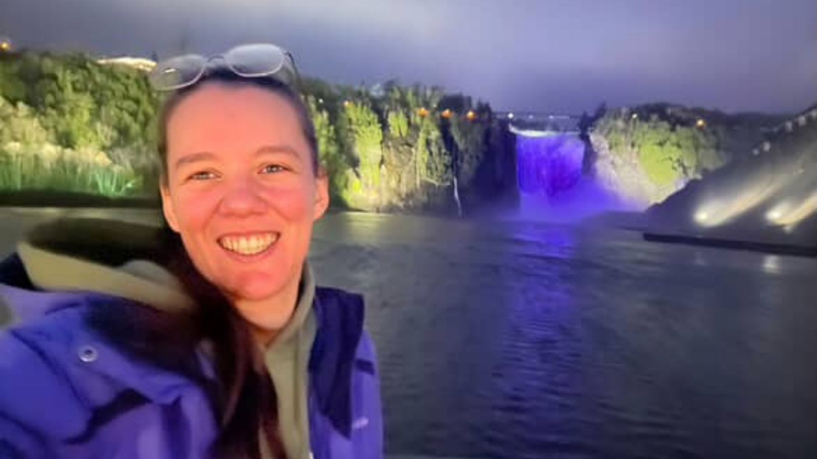 Personne souriante prenant un selfie devant une cascade illuminée en violet la nuit, symbolisant la prise de conscience du lupus.