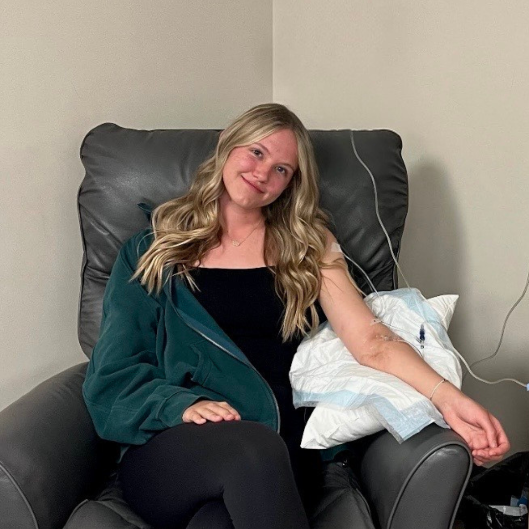 Photo of Victoria Fraser, Lupus Canada Scholarship Winner, seated during a medical treatment with IV in arm.