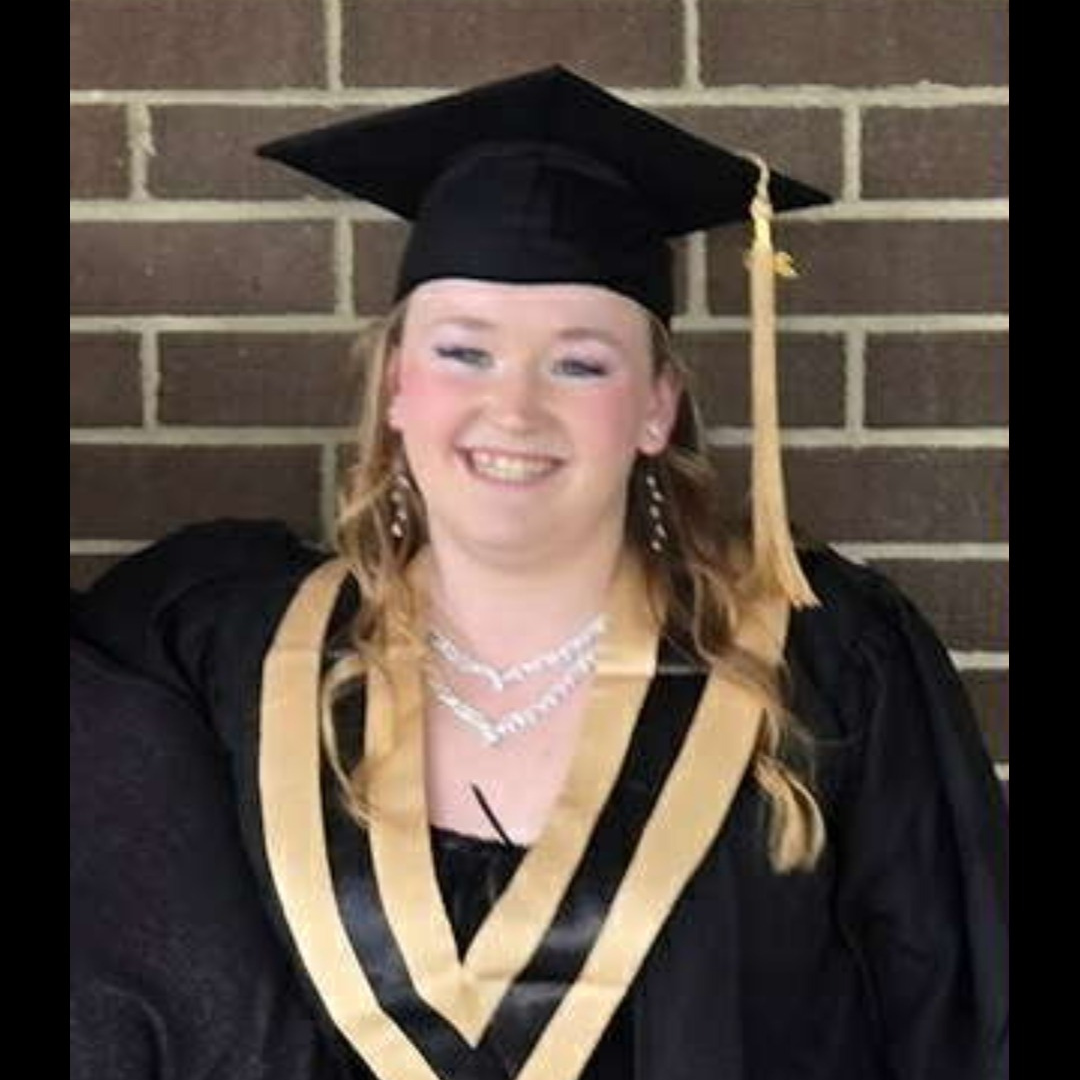 Young woman smiling in a graduation cap and gown with a gold and black stole.