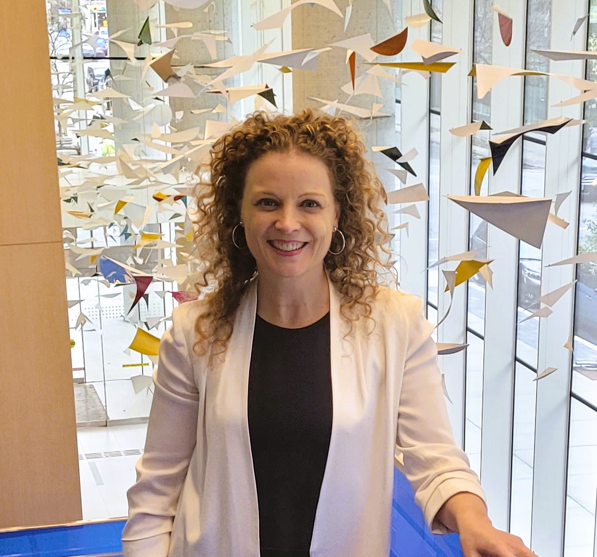 Étude BIONIC – Produits biologiques dans la grossesse lupique Portrait d’une femme debout à l’intérieur devant une sculpture suspendue colorée, utilisée pour une page de recherche sur les produits biologiques dans la grossesse lupique.