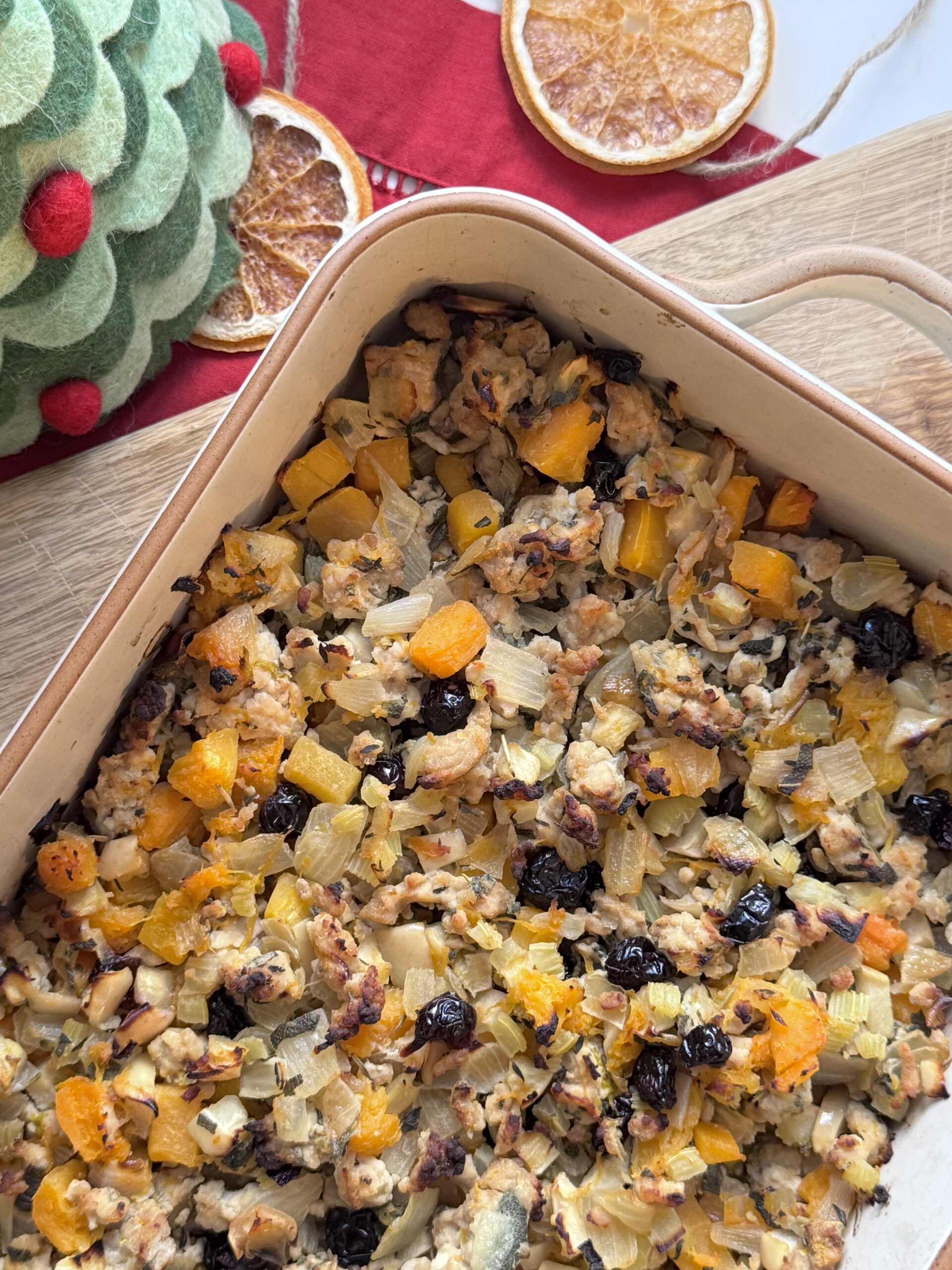 Farce sans céréales dans un plat à gratin avec courge, dinde, herbes et fruits secs, coiffé sur une table de fête.