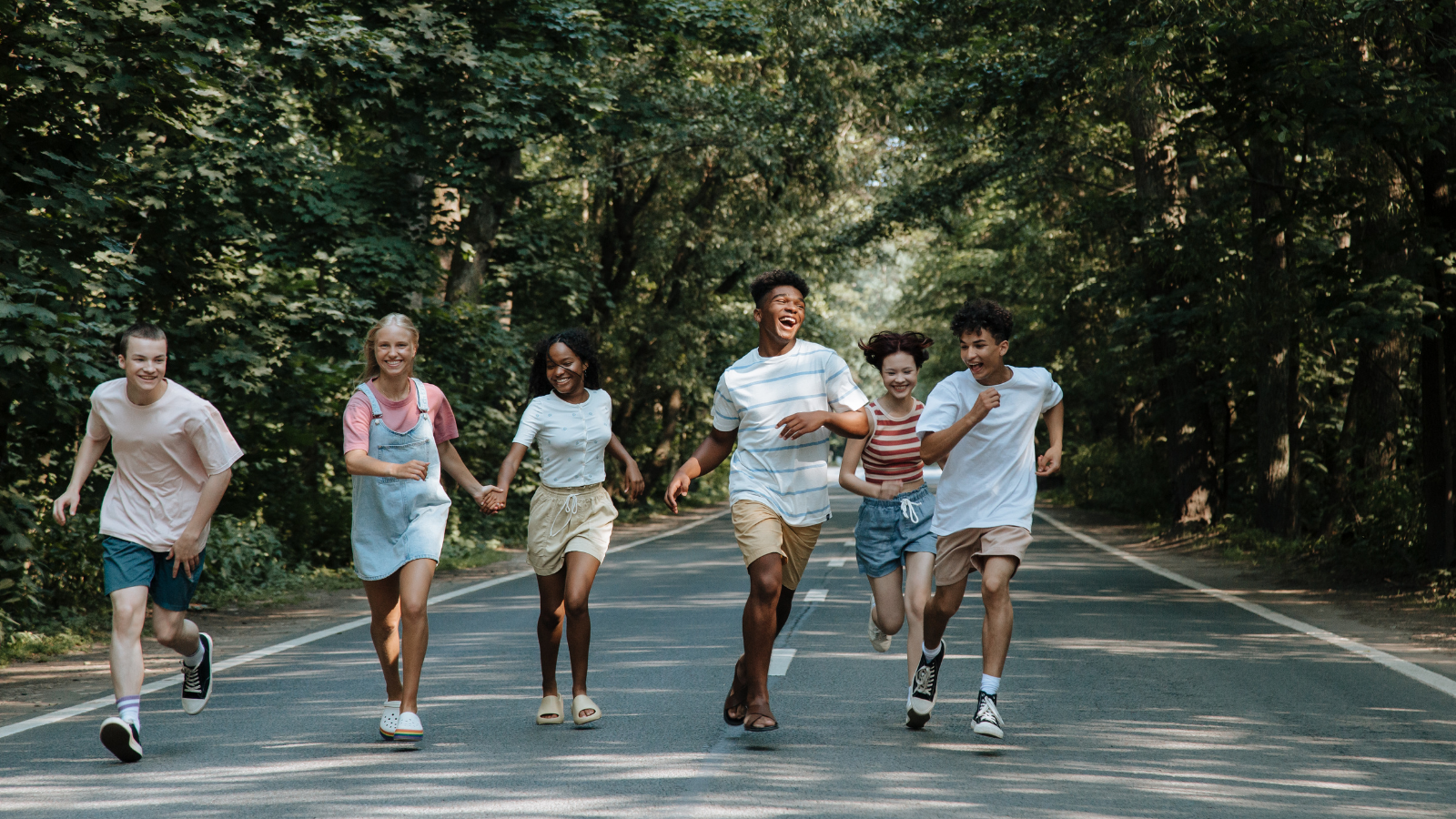 Un groupe diversifié d’adolescents et de jeunes adultes courant et riant ensemble sur une route boisée, symbolisant la jeunesse, l’énergie et l’importance de rester en bonne santé.