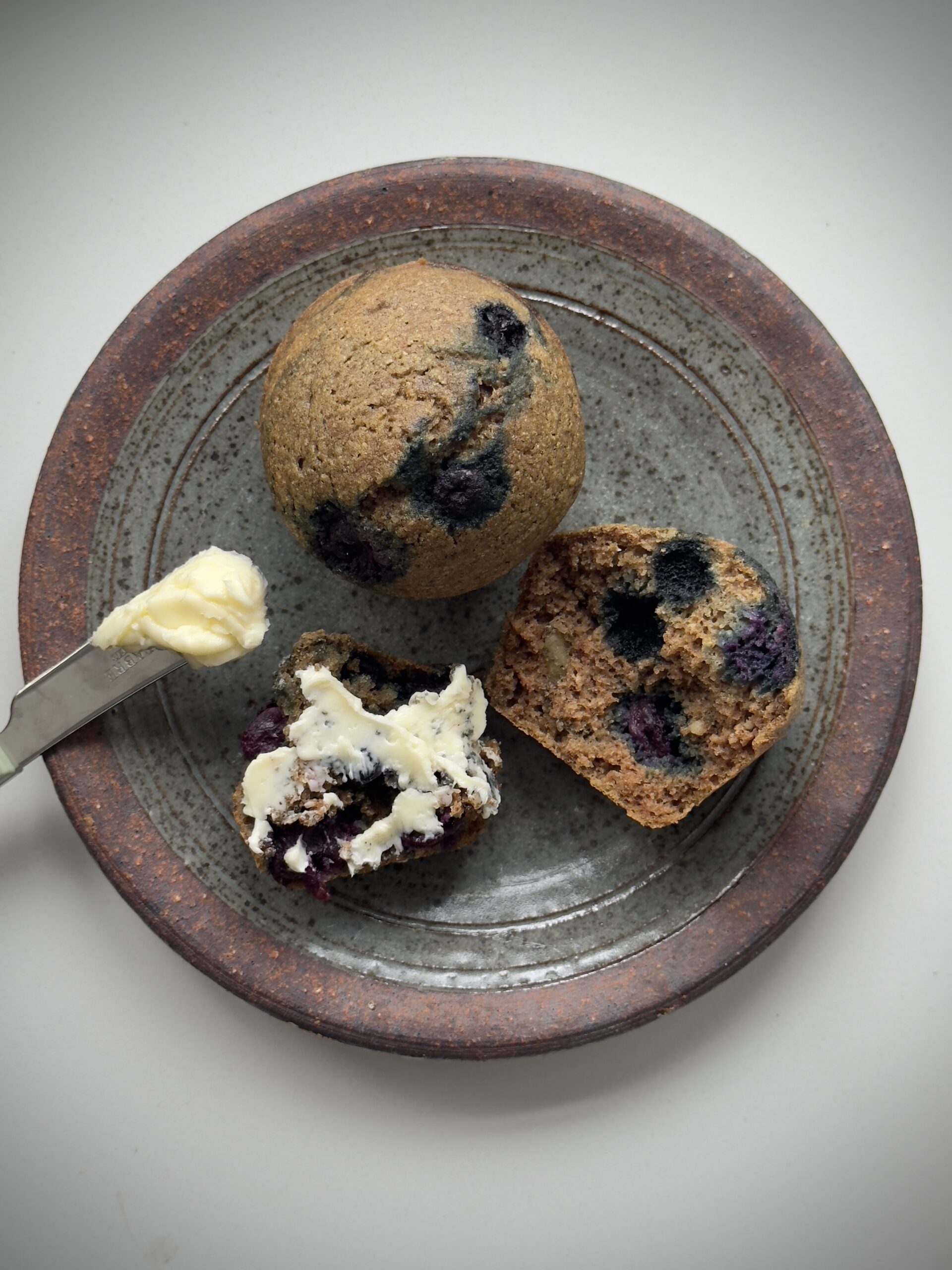 Buckwheat blueberry muffins served on a plate, one cut open to show the soft texture and blueberries inside
