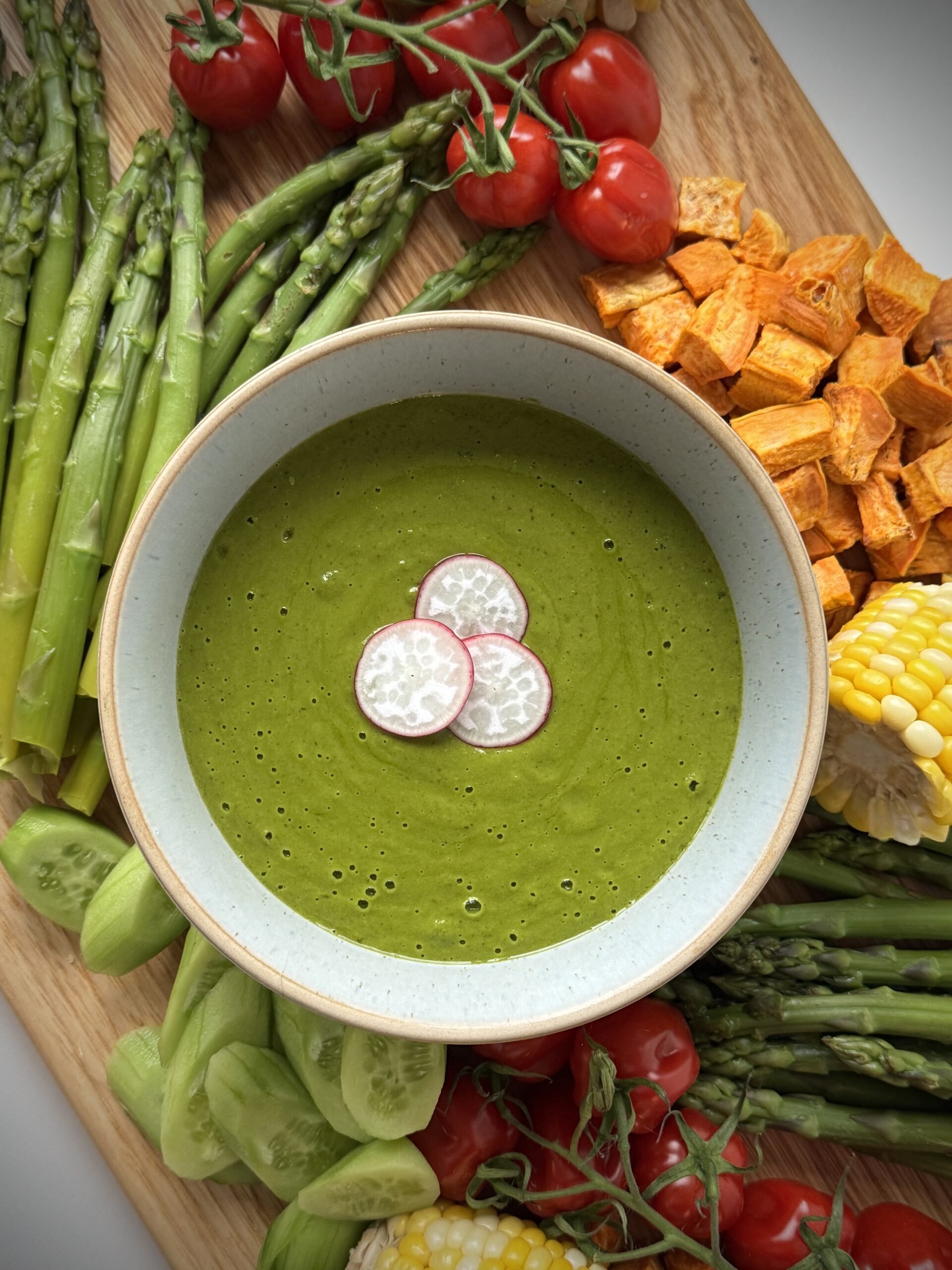 Green Herb Sauce Recipe served in a bowl with fresh asparagus, cucumbers, cherry tomatoes, sweet potatoes, and corn